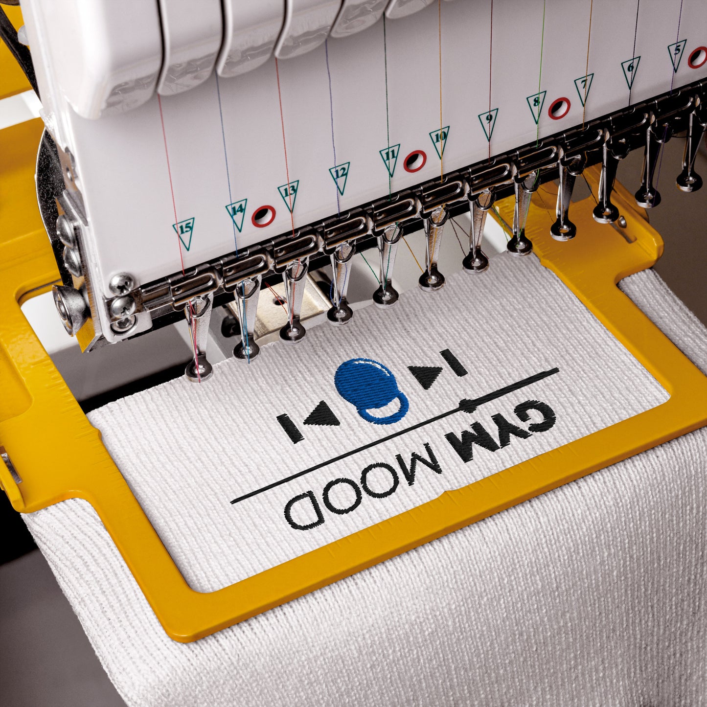 Embroidery machine stitching the Gym Mood On beanie with black text and blue kettlebell design on white fabric.