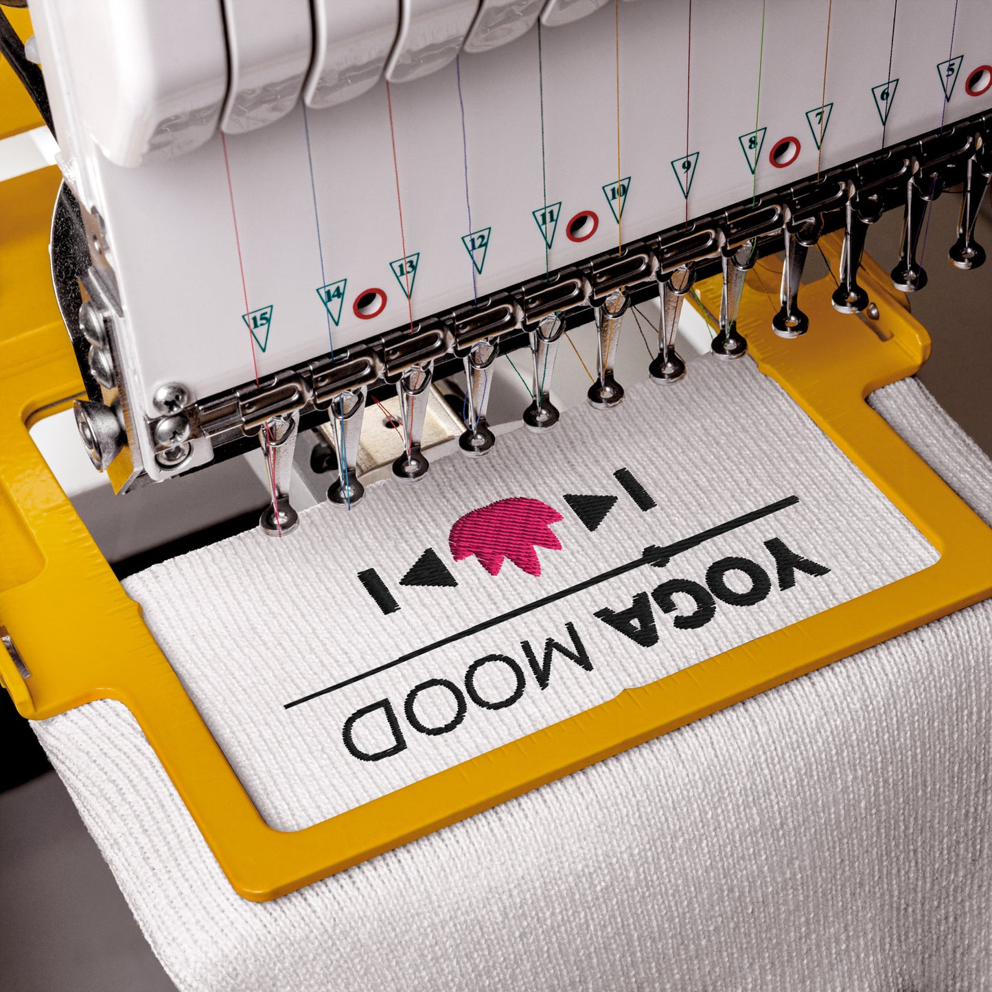 Embroidery machine stitching the Yoga Mood On beanie with black text and pink lotus design on white fabric.