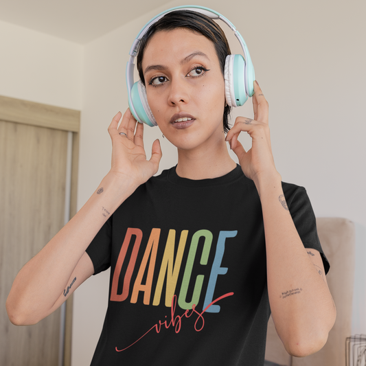 Person wearing colorful 'DANCE vibes' t-shirt and light blue headphones indoors.
