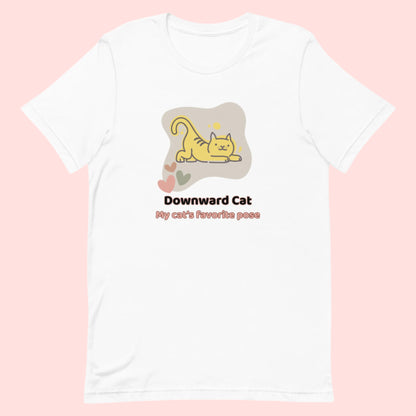 White unisex yoga t-shirt featuring a playful cartoon illustration of a cat doing a yoga stretch, paired with the text “Downward Cat: My Cat’s Favorite Pose.” 