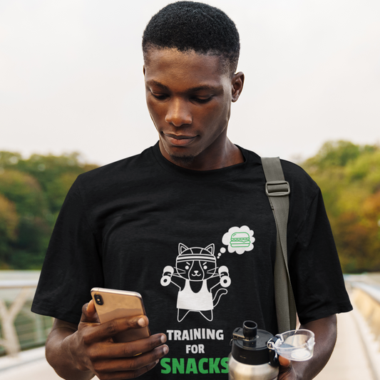 Person wearing a black gym t-shirt with a phrase " Training for Snacks" and text, holding a phone and water bottle outdoors.