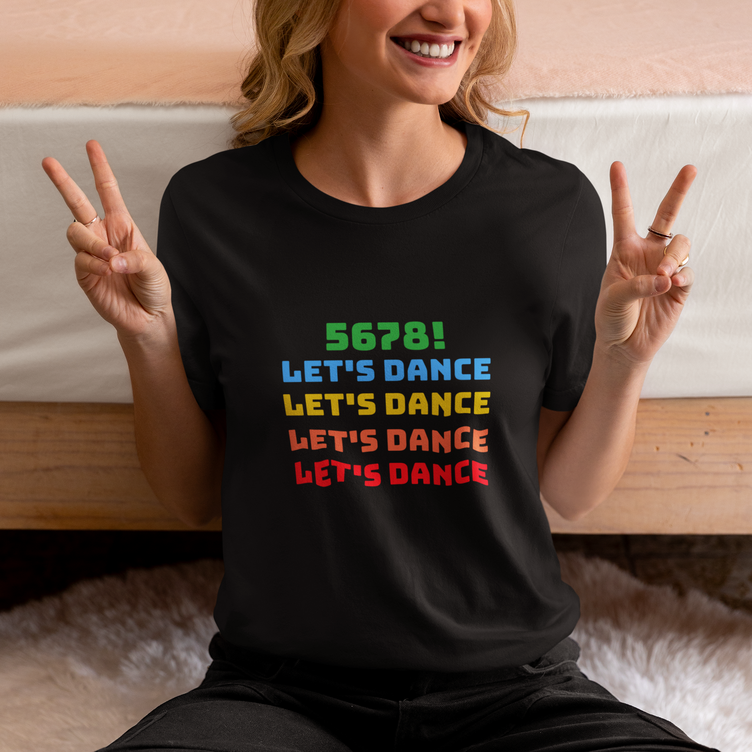 Woman wearing black unisex dance tee shirt with colorful "5678! Let's Dance" stacked text in green, blue, yellow, orange, and red.