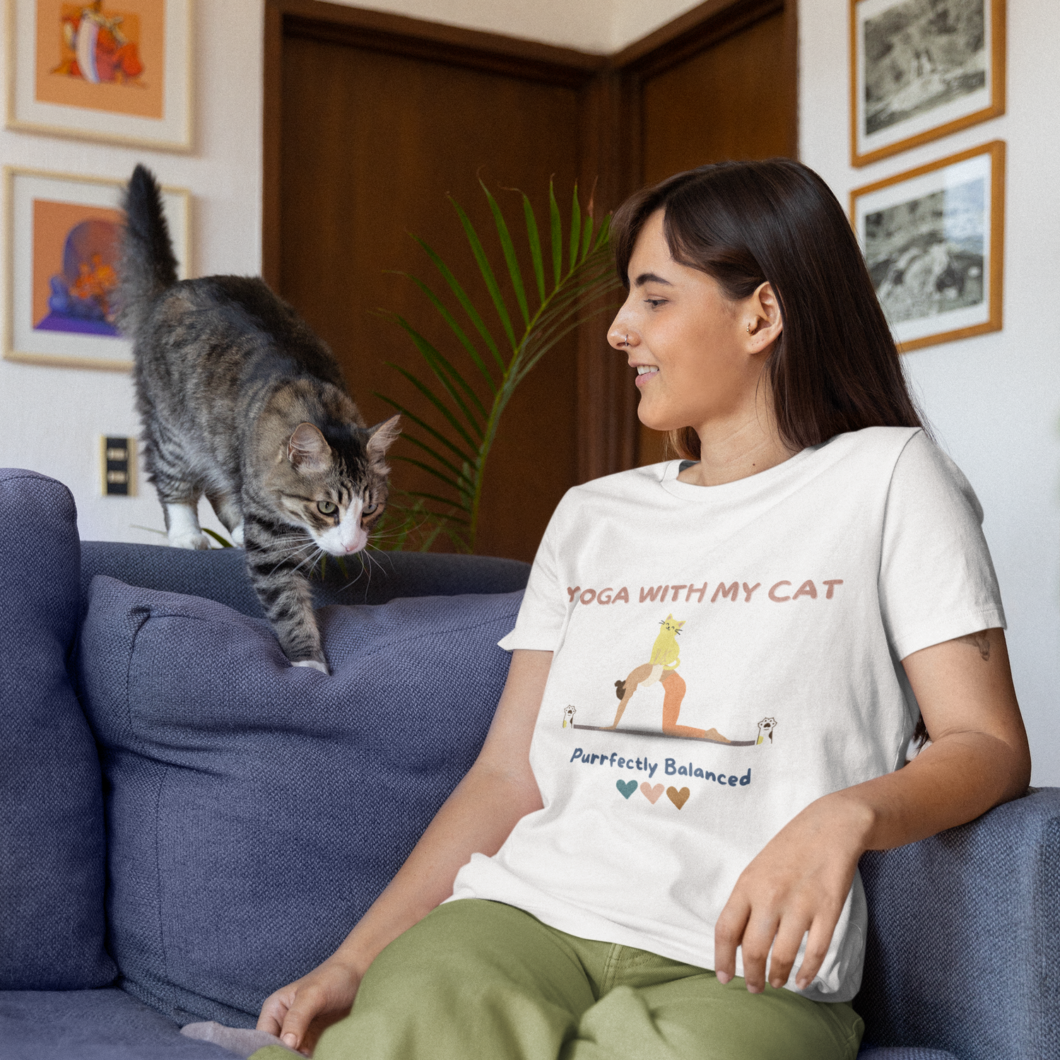 Woman sitting on a couch with a cat and wearing a yoga t-shirt that says 'Yoga with my cat purrfectly balanced'