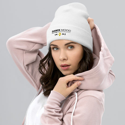 Woman wearing a white Dance Mood On beanie with black text and yellow music note embroidery, paired with a light pink hoodie on a gray background.
